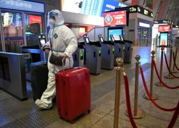 TERDAPAT penumpang sanggup memakai sut perlindungan diri (PPE) sebagai langkah pencegahan jangkitan Covid-19 ketika beratur di salah sebuah stesen kereta api di Beijing, China. -AFP