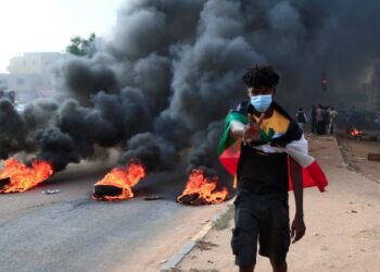 PESERTA protes meletakkan bendera Sudan di bahu dan kelihatan tayar yang dibakar semasa demonstrasi di Khartoum.-AFP