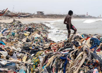 SEORANG lelaki berdiri atas timbunan pakaian terpakai yang dilambakkan di tepi pantai di Accra, Ghana. - SHUTTERSTOCK