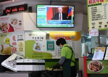 SEORANG peniaga wanita memotong sayur di sebuah restoran di Hong Kong, semasa Vladimir Putin
muncul dalam siaran berita televisyen. - AFP