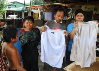 MUHAMMAD Saifudin Abdul Rahman, Roshaslinda Makhtar dan anak mereka, Muhammad Hasif menunjukkan pakaian sekolah yang rosak akibat banjir di Kampung Sepakat Baru, Skudai, Johor. - UTUSAN/RAJA JAAFAR ALI