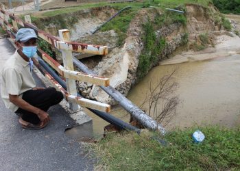 IBRAHIM Ishaq menunjukkan hakisan sungai yang menyebabkan struktur jambatan berkenaan rosak sehingga mengundang risiko penduduk terputus hubungan di Kampung Padang Lebar, Kota, dekat sini, semalam.-UTUSAN/NOR AINNA HAMZAH