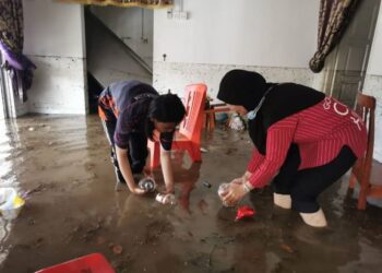 NUR ASYIKIN Kasmun (kiri) dan Rosnani Ahmad mengangkat bekas kuih raya yang terapung dalam air banjir di rumah mereka di Kampung Sungai Putat, Bukit Beruang, Melaka. - UTUSAN/DIYANATUL ATIQAH ZAKARYA