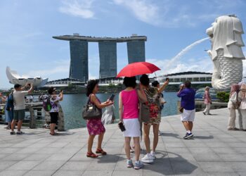 PARA pelancong bergambar di hadapan mercu tanda Merlion di Marina Bay, Singapura. - AFP