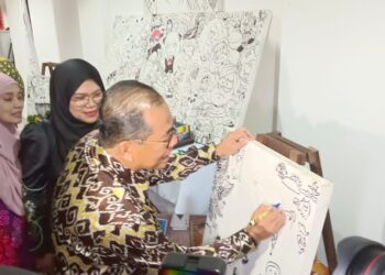 MOHAMED KHALED NORDIN melukis pada kanvas karikatur ketika mengadakan lawatan ke PIS di Pasir Gudang.