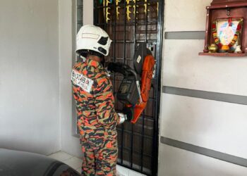 ANGGOTA bomba menggunakan peralatan khas untuk membuka pintu rumah lelaki warga emas yang ditemukan meninggal dunia di Lahat, Ipoh hari ini. - UTUSAN/IHSAN JBPM