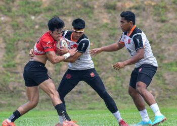 PEMAIN Bunga Raya 7s, Adam Ariff Alias (tengah) cuba melepasi kawalan pemain Singapura 7s pada perlawanan ujian di Stadium Ragbi Kompleks Sukan Johor, Mount Austin, Johor Bahru.