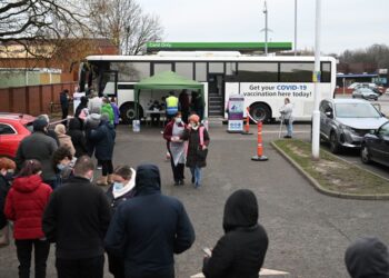 PENDUDUK beratur untuk menerima suntikan vaksin Covid-19 di sebuah pusat pemberian vaksin (PPV) bas bergerak yang ditempatkan di kawasan parkir luar Pasar Raya Asda di Farnworth, barat laut England. - AFP