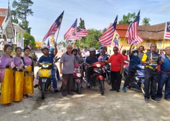 PIM Chau Dam (baju merah) melekatkan Jalur Gemilang di motosikal peserta konvoi di pekarangan Wat Phikulthong Vararam Kampung Terbak, Tumpat, Kelantan semalam. – UTUSAN/ROHANA ISMAIL