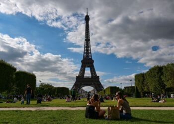 PENGUNJUNG duduk bersantai di Champ de Mars di hadapan Menara Eiffel di Paris. - AFP 