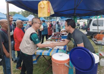 RAZALI Idris (kiri) menyantuni penduduk dan peniaga di pasar malam Kijal, Kemaman, semalam. -  UTUSAN/NIK NUR IZZATUL HAZWANI NIK ADNAN