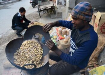 PENJUAL sedang memanggang kacang di gerai tepi jalan di Amritsar, India. - AFP 