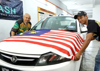 ABDUL Salim Putera Ahmad Shibi (kiri) menyerahkan Jalur Gemilang kepada pelanggannya di Pusat Cucian Kenderaan Kazoku di Pekan Razaki, Ipoh. – UTUSAN/MUHAMAD NAZREEN SYAH MUSTHAFA