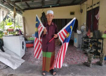 SHAARI Mokri memegang Jalur Gemilang ketika menceritakan pengalaman ketika negara berdepan ancaman komunis di Sungai Manik, Pasir Salak, baru-baru ini. – UTUSAN/AIN SAFRE BIDIN