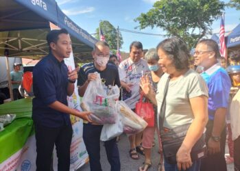 FAHMI Zainol (kiri) mengedarkan sayur percuma kepada orang ramai sempena program Jualan Agro Madani di kawasan DUN Pantai Jerejak, Bayan Lepas, Pulau Pinang hari ini.