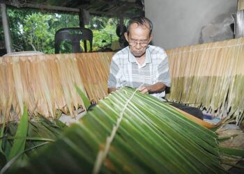 HASHIM Din mengikat daun rumbia menggunakan kulit pokok bemban di rumahnya di Kampung Kubang Gajah, Arau, Perlis. - UTUSAN/IZLIZAN OTHMAN