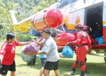 PENDUDUK kampung membantu menurunkan bakul makanan di Pekan Pensiangan, Sabah, semalam.