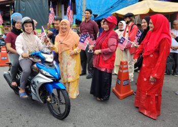 HAFIDZAH Mustakim (tiga dari kiri) ketika mengedarkan Jalur Gemilang kepada pengguna jalan raya yang melalui kawasan Pasar Kubang Pasu di Kota Bharu, Kelantan hari ini. UTUSAN/MUSTAQIM MOHAMED