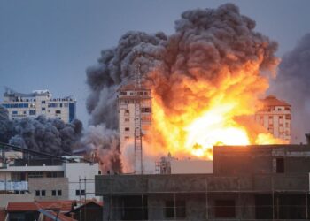 Orang ramai berdiri di atas bumbung melihat  api marak dengan asap tebal yang memusnahkan Menara Palestin akibat  dibedil  pasukan udara Israel di Gaza,  Sabtu lalu.  – AFP