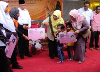 HALIMATON Shaadiah Saad (tengah) menyampaikan replika kad OKU kepada kanak-kanak kembar yang mendaftar dengan JKM pada Program Semai Bakti Santuni dan Sayangi OKU bersama Penduduk Orang Asli Kensiu di Ulu Legong, Baling.