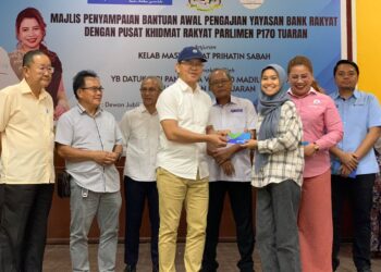 WILFRED (lima, dari kanan) dan Philip (empat, dari kanan) menyampaikan sumbangan kepada salah seorang penerima bantuan di Sekolah Menengah Kebangsaan Tamparuli, Sabah hari ini.