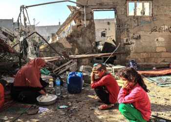 SEORANG wanita membancuh tepung untuk membuat roti sambil disaksikan oleh dua cucunya di celah runtuhan rumah mereka di Rafah, selatan Semenanjung Gaza. - AFP