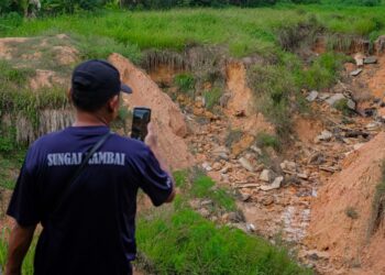 SUHAIMI Ahmad mengambil gambar lokasi hakisan tanah yang membentuk kawah di Taman LKP, Jasin, Melaka. - UTUSAN/SYAFEEQ AHMAD