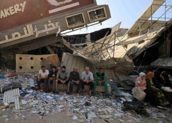 Penduduk Gaza duduk di hadapan runtuhan kilang roti yang musnah dibom Israel.- AFP