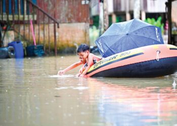 DUA kanak-kanak bermain air banjir sambil menaiki sebuat bot di Pengkalan Ajal, Hulu Terengganu, semalam. –  UTUSAN/PUQTRA HARRY ROSLI