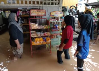 ENGKU Hasmah Engku Kamaruzaman (kiri) tetap menjalankan perniagaan walaupun premisnya dinaiki air dalam kejadian banjir di Kampung Nibong, Hulu Terengganu, semalam. - UTUSAN/NOOR HAYATI MAMAT