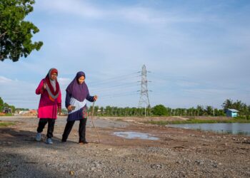 RABIAH Samah (kanan) terpaksa membawa kayu sebagai langkah berjaga-jaga ketika berjoging di Kolam Takungan Banjir Semabok, Melaka. - UTUSAN/SYAFEEQ AHMAD