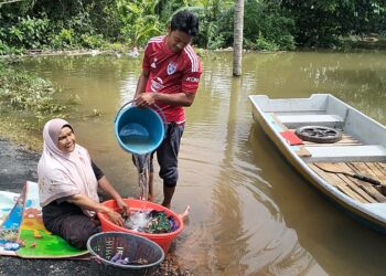 FAUZIAH Che Daud (kiri) membasuh pakaian di halaman rumahnya yang masih ditenggelami banjir di Kampung Tersang Rantau Panjang, Kelantan-UTUSAN/ROHANA ISMAIL.