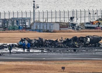 PEGAWAI penyiasat berdiri berhampiran bangkai pesawat pengawal pantai Jepun di landasan Lapangan Terbang Haneda, Tokyo. - AFP 