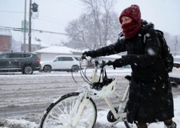 SEORANG wanita membawa basikal menyeberang jalan raya yang dipenuhi salji di Chicago.-AGENSI