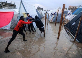 BEBERAPA pelarian Palestin mengelak daripada memijak air limpahan hujan di sebuah kem sementara di Rafah di selatan Gaza.-AFP