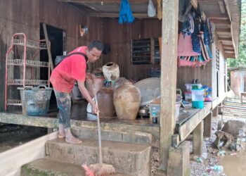 SEORANG penduduk membersihkan lumpur di rumahnya akibat banjir di Kampung Pasir Raja, Hulu Dungun, Dungun, semalam. - UTUSAN/NIK NUR IZZATUL HAZWANI NIK ADNAN