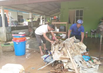 M. HAIRUDIN Yasin (kiri) dan saudaranya membersihkan kediaman yang dinaiki air akibat banjir di Kampung Maju Jaya, Jalan Kempas Lama, Johor Bahru.