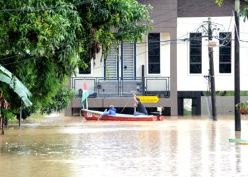 DUA beranak menaiki bot ke rumah mereka yang dilanda banjir berikutan hujan lebat di Kampung Paya Kenangan di Desa Mutiara, Johor Bahru.