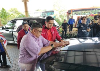 AB. RAUF Yusoh (kiri) menampal pelekat Misi Bantuan Banjir Johor di sebuah kereta selepas Pemukiman Wanita UMNO Bahagian Jasin di A’Famosa Resort, Alor Gajah, Melaka.