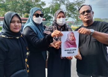 NORHISHAM Samsusah (kiri) bersama keluarganya memegang poster menuntut keadilan atas kematian adiknya Bella ketika hadir di Mahkamah Majistret Batu Pahat, semalam.