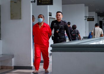 TERTUDUH yang memakai baju banduan diiringi keluar anggota polis selepas dihadapkan ke Mahkamah Majistret dan Mahkamah Sesyen, Ayer Keroh, Melaka atas pelbagai pertuduhan jenayah. - UTUSAN/SYAFEEQ AHMAD