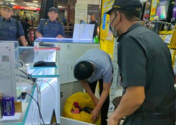 ANGGOTA KPDN Perak memeriksa barangan yang dirampas dalam serbuan di dua kedai dalam kompleks membeli-belah di Jalan Laksamana, Ipoh kerana disyaki menjual telefon bimbit dan aksesori tiruan, semalam. - UTUSAN/IHSAN KPDN