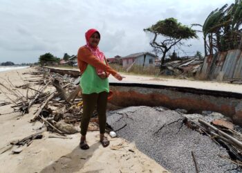 AZIZAH Husin menunjukkan keadaan jalan di hadapan kediamannya yang runtuh akibat hakisan pantai di Kampung Pachakan di Kuala Besut, Besut,- UTUSAN/WAN ZURATIKAH IFFAH WAN ZULKIFLI