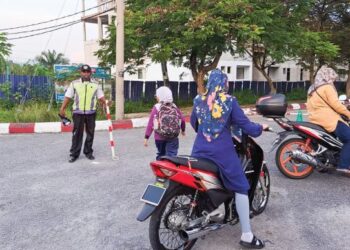 K. KITTU mengawal lalu lintas semasa ibu bapa menghantar anak mereka ke Sekolah Kebangsaan (SK) Bandar Baru Putera, Bercham, Ipoh semalam. – UTUSAN/SAYED HESHAM IDRIS