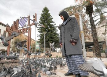 SEORANG wanita berdiri di antara burung merpati di Dataran Luar Basilika Pengumuman Katolik Roma di Nazareth, utara Israel pada 31 Januari 2024.-AFP