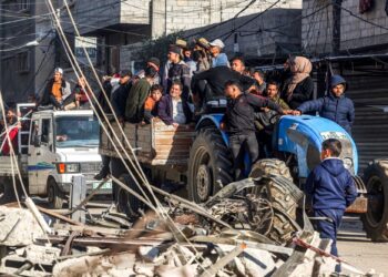 PENDUDUK menaiki kereta yang ditarik oleh traktor melepasi menara masjid yang musnah di Rafah di selatan Semenanjung Gaza.-AFP