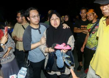 Ibu saudara menunjukkan kasut dan pakaian anak saudaranya semasa satu lagi mangsa dijumpai dalam kejadian kepala air di Sungai Kenjur dekat Kampung Poh, Bidor  pukul 9.50 malam kelmarin. -UTUSAN/MUHAMAD NAZREEN SYAH MUSTHAFA