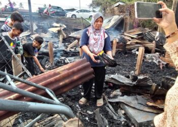 NORHAYATI Ibrahim menunjukkan buku teks milik anaknya yang hangus dalam kejadian di Kampung Banggol, Kota Bharu, Kelantan-UTUSAN/ROHANA MOHD. NAWI.