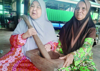 HABSAH Abdullah (kiri) menyerahkan lesung tangan kayu kepada Asmah Abdul Rahman di Galeri Awla Pondok Pok Kob, Chenor di Maran, Pahang. - UTUSAN/SALEHUDIN MAT RASAD