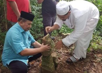 MOHAMED Ariffin Awang Ismail (duduk) turut membetulkan batu nisan berukiran Acheh yang dipercayai milik Puteri Berdarah Putih di Kampung Gulun, Chenor, Pahang.